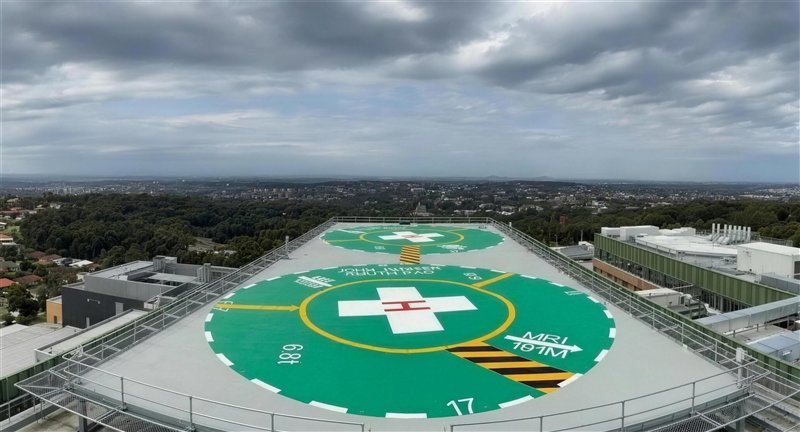John Hunter Hospital rooftop helipads with green pads, white crosses and hazard striping, overlooking the city